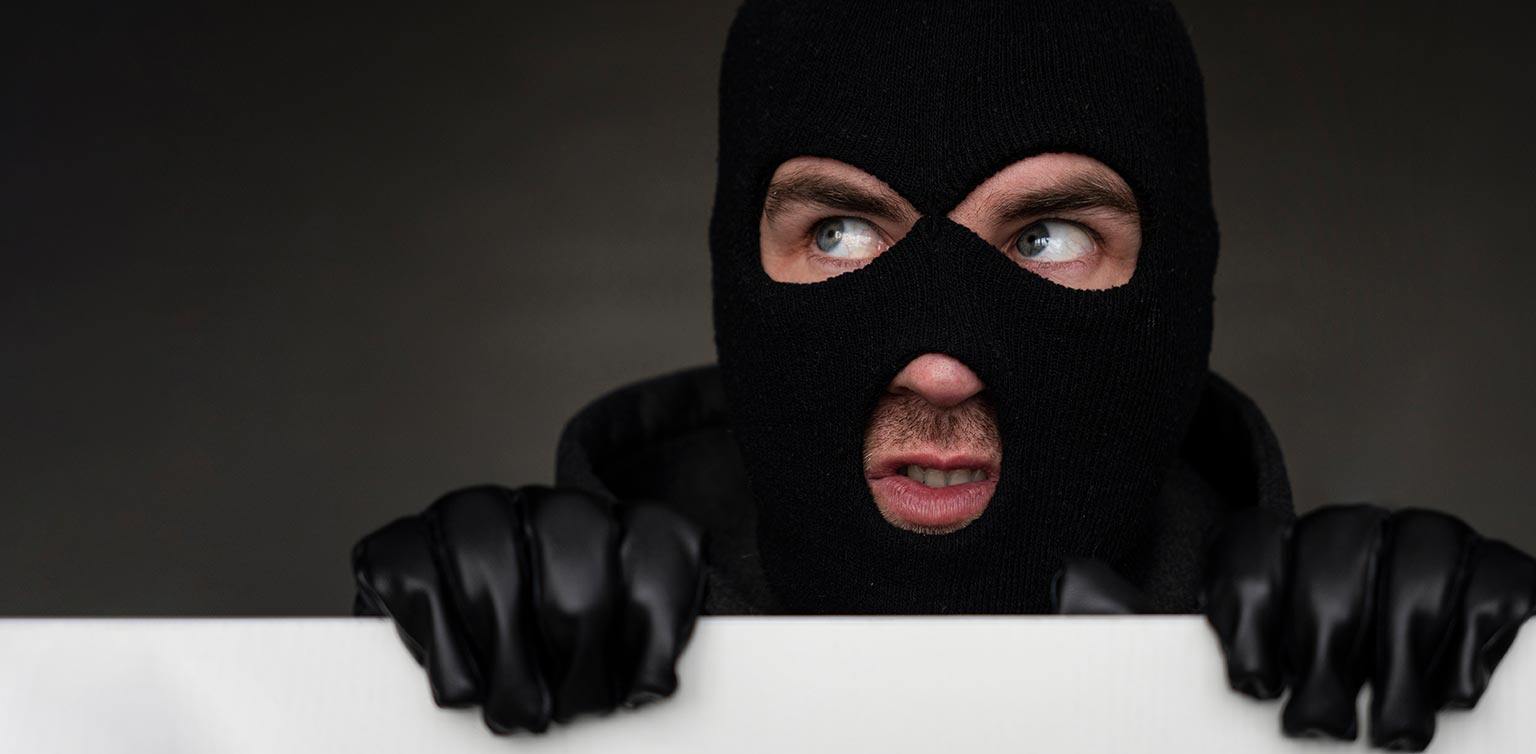 A photo of a man wearing a black balaclava and gloves peering over a white fence