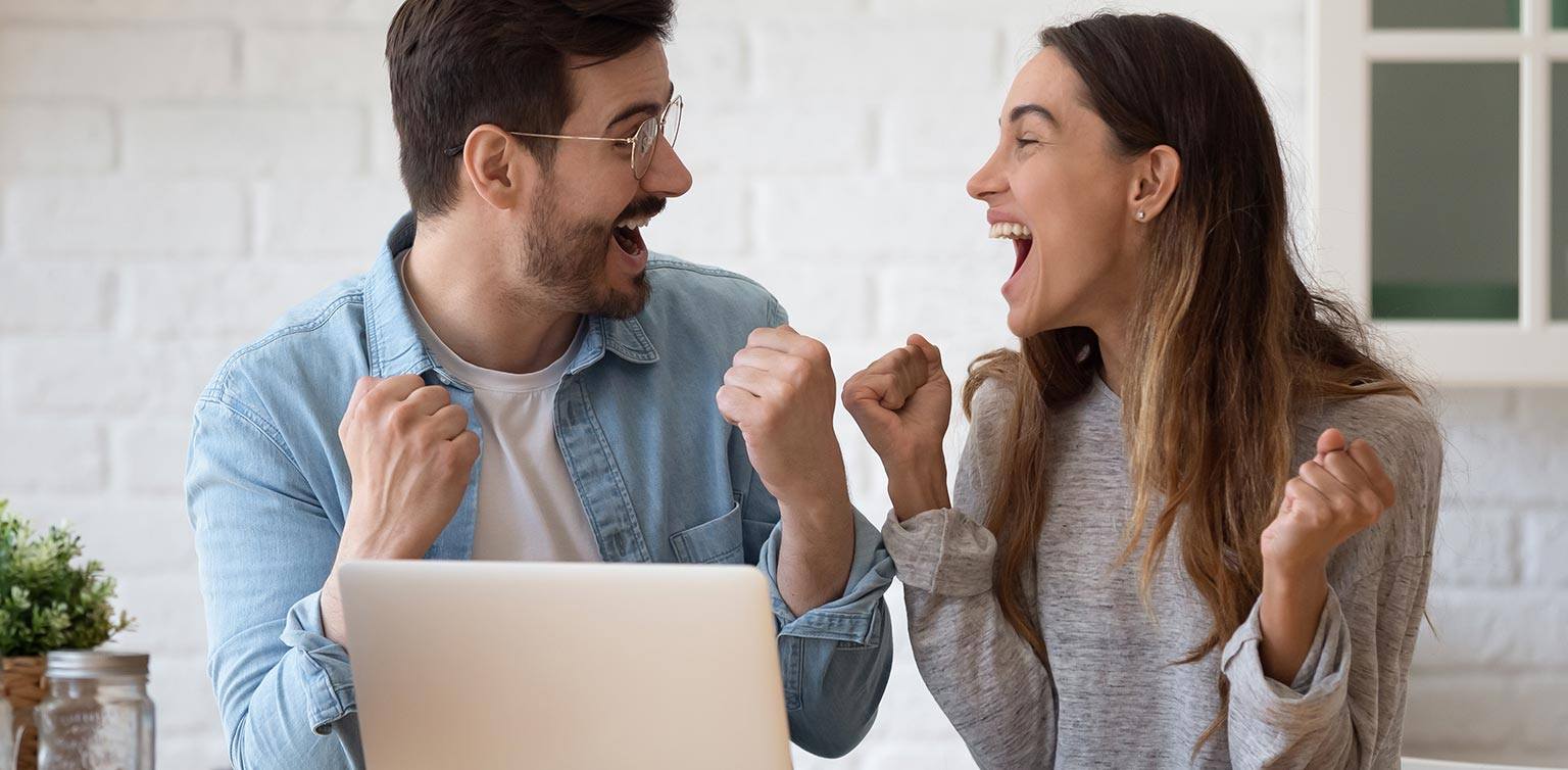 A photo of a happy man and woman sitting in front of a laptop yelling with joy