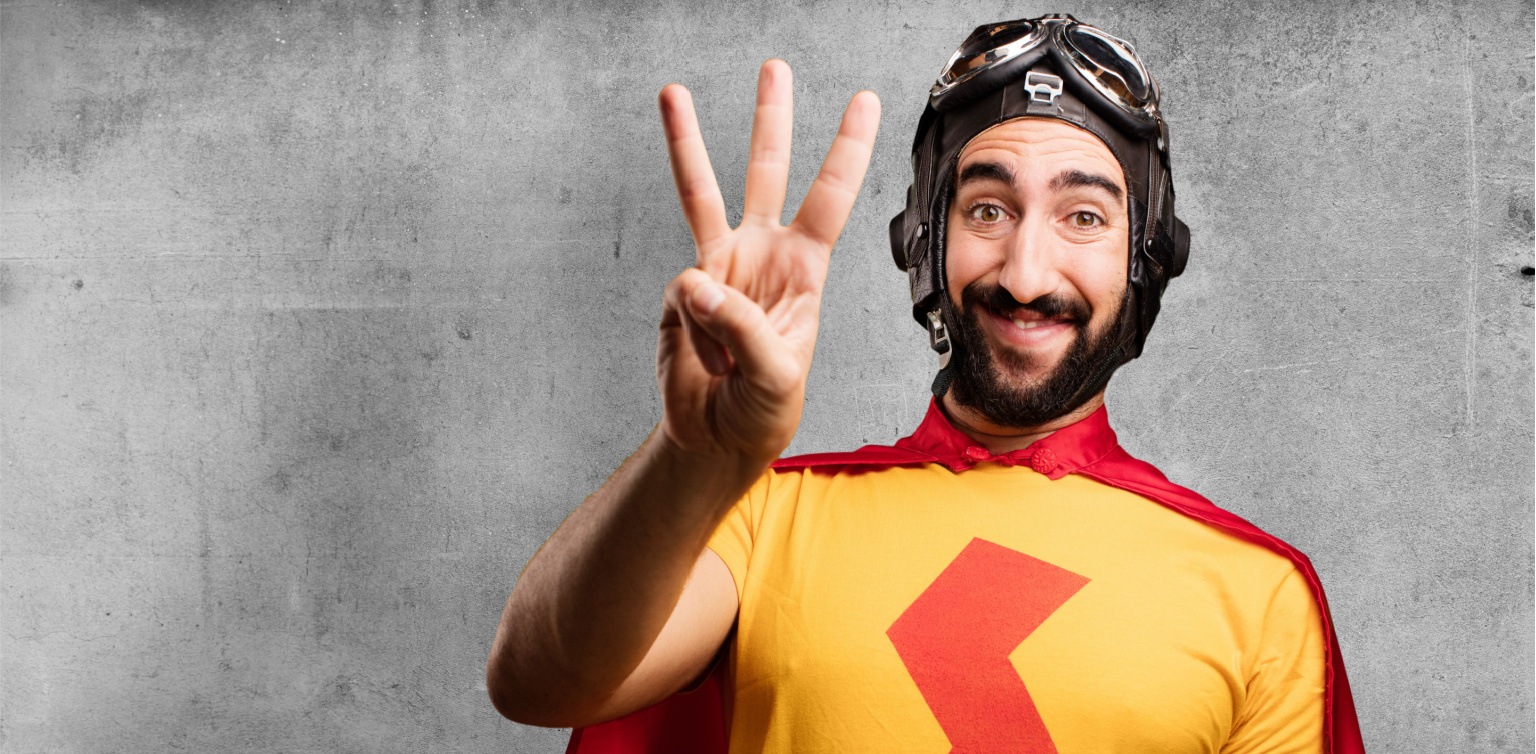 A man in a superhero outfit holding up his hand with three fingers on a grey background 