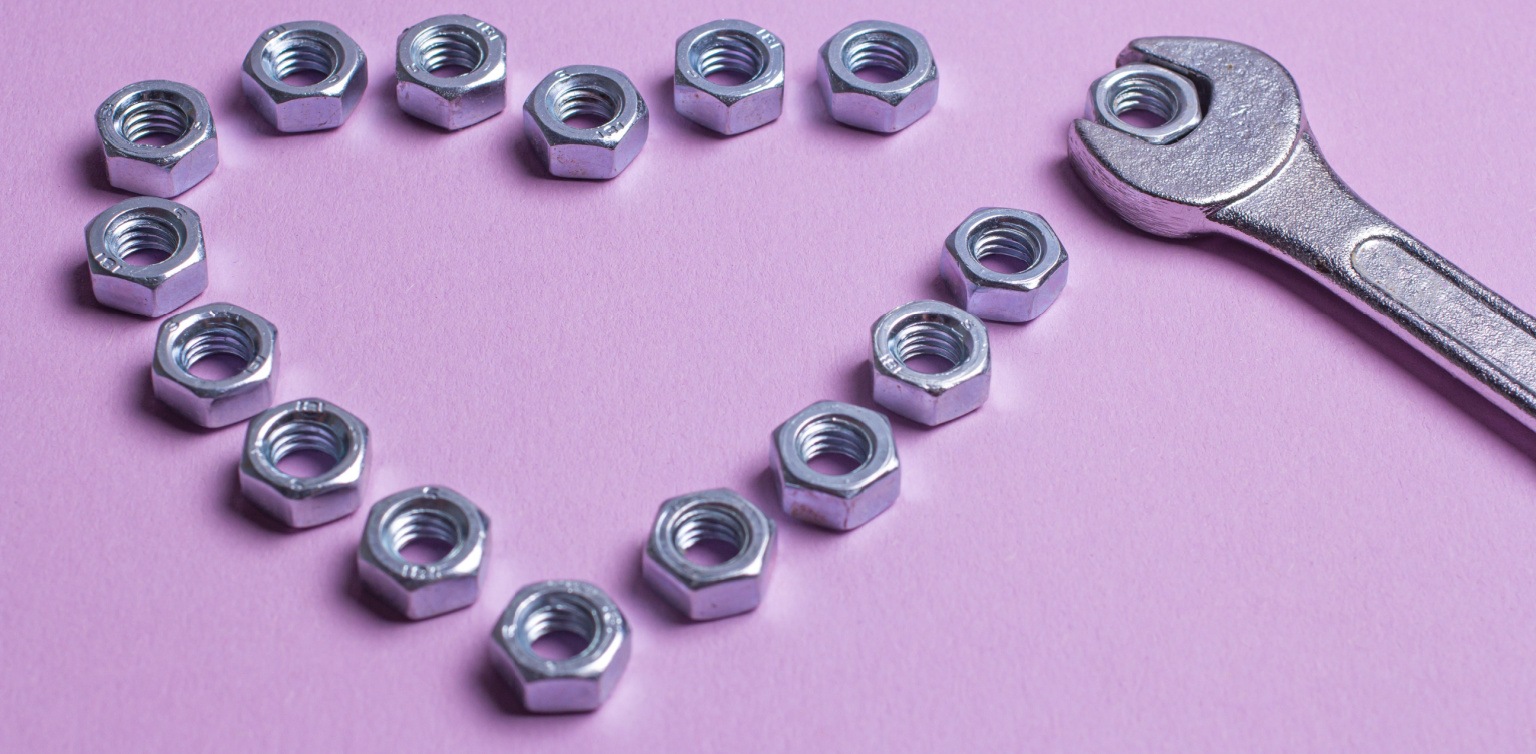 Bolts in the shape of a heart with a wrench gripping one bolt on a light purple background