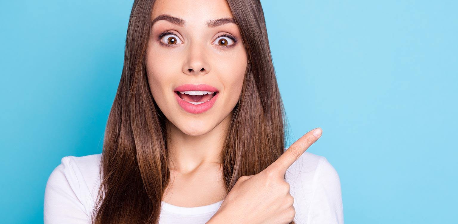 A photo of a happy looking dark-haired woman pointing at something as a recommendation on a light blue background