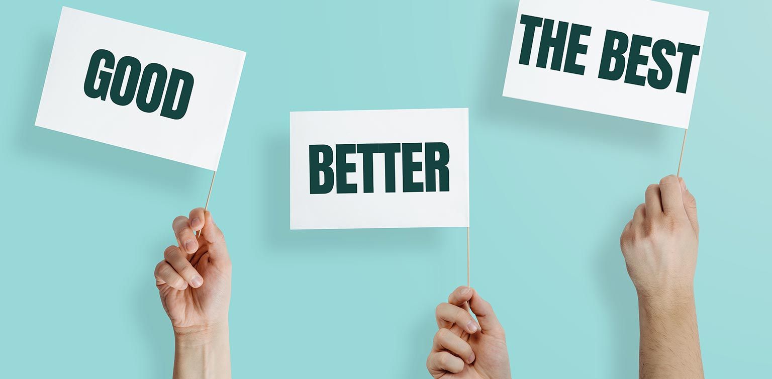 A photo of hands holding 3 white flags with ‘Good’, ‘Better’, ‘Best’ against a light blue background