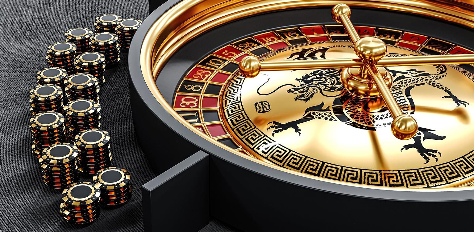 A black and gold roulette wheel with a dragon design and stacks of poker chips on a grey felt surface 